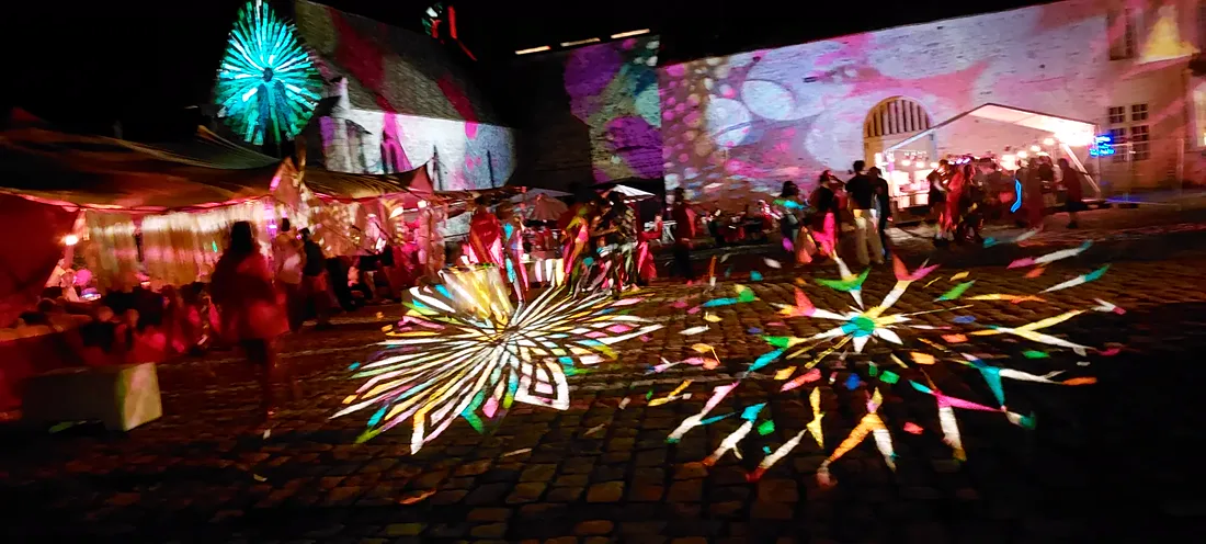 Chão de calçada portuguesa coberto por duas rosáceas de luz colorida projetadas, à noite.